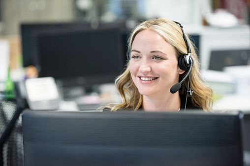 Mid adult woman working in call centre, businesswoman on a call wearing headphones and microphone