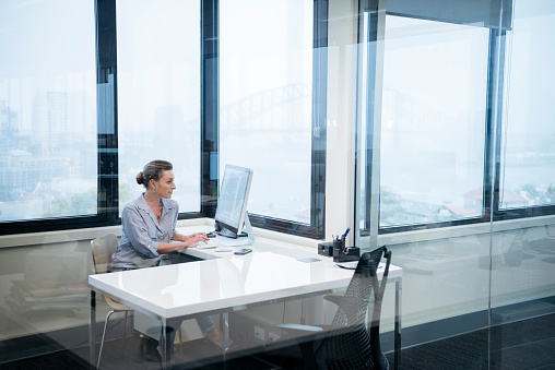 Businesswoman sitting at desk behind glass in modern office