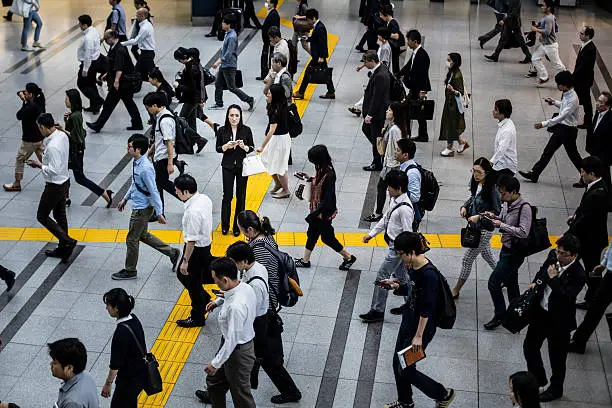 Photo of Japanese woman talking on the mobile phone surrounded by commuters