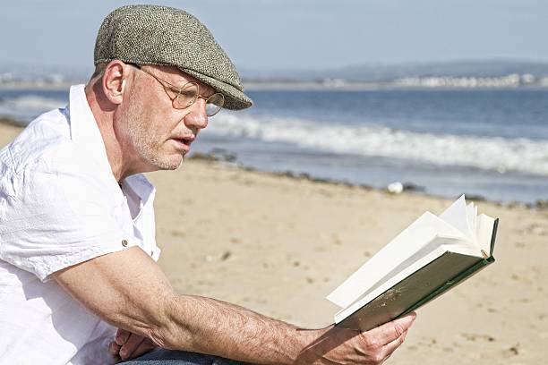 istock mature man reading at the beach 604342732
