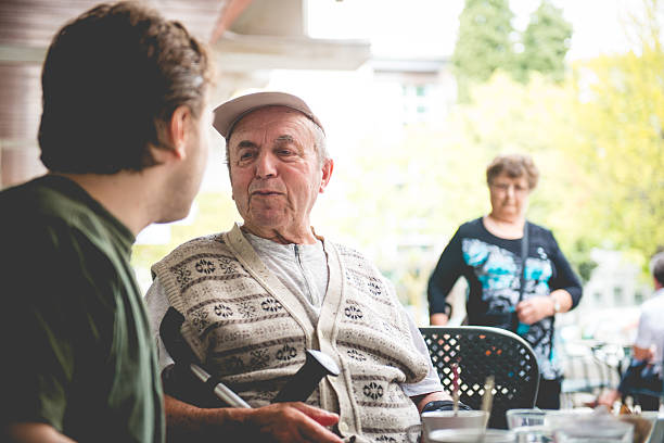 Happy Senior Man in Wheelchair and Grandson Having Coffee, Europe A happy disabled senior man and a happy male nurse, grandson, having coffee at the Cafe Trieste in the city centre, Slovenia, Europe. Senior woman is walking towards them.. Nikon D800, full frame, XXXL. primorska stock pictures, royalty-free photos & images