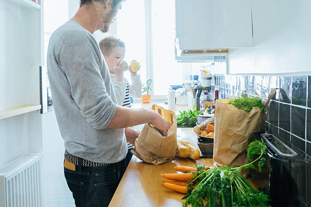 padre e figlio organizzazione di generi alimentari in cucina - paper bag groceries food vegetable foto e immagini stock