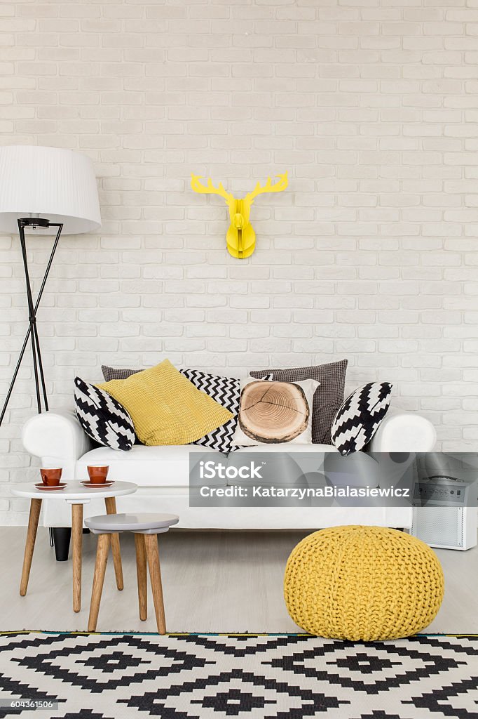 Comfortable sofa corner in a contemporary flat Stylish white sofa filled with pillows in a modern lounge room with white brick wall, decorative carpet and a lamp Yellow Stock Photo