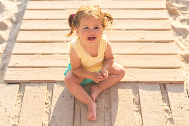 niña sentada en un camino de madera en una playa - beach family boardwalk footpath fotografías e imágenes de stock