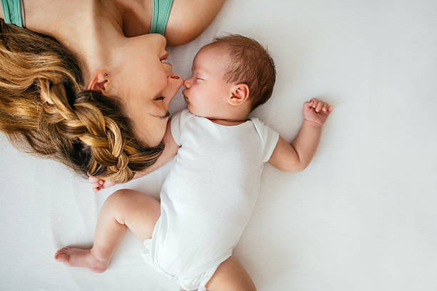 Motherhood Young mother and her newborn baby are lying down and cuddling  2 5 months stock pictures, royalty-free photos & images