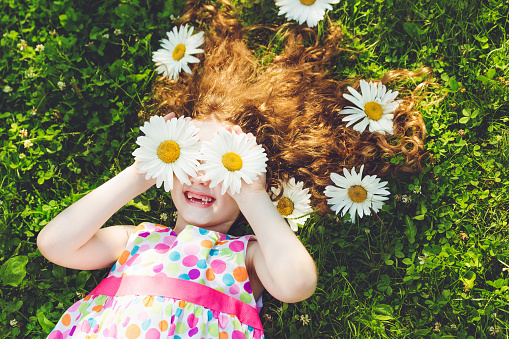 Child with daisy eyes with rainbow dress lying on green grass in a summer park.