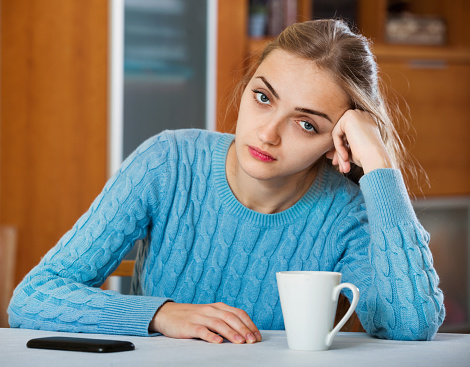 Upset adult girl in blue sweater waiting for important call