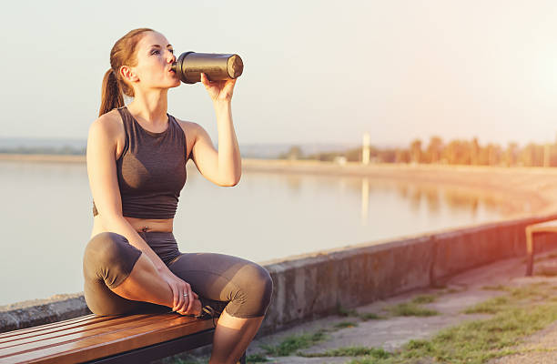 Young girl with a shaker water outdoors Young girl running after sitting on the bench. Sportswoman drinks from the shaker. protein drink stock pictures, royalty-free photos & images