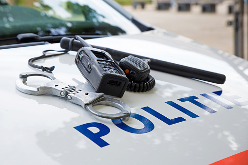 Police equipment on a dutch police car.  Handcuffs, baton and phone on top of a police car. Selective focus