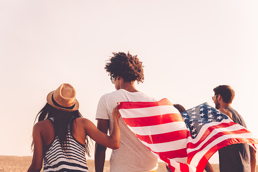 Rear view of four young people carrying american flag while running outdoors