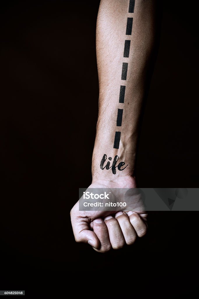 dashed line and word life in a forearm closeup of a young caucasian man with a dashed line and the word life simulating a tattoo in his forearm, against a black background Forearm Stock Photo