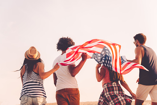 Rear view of four young people carrying american flag while running outdoors