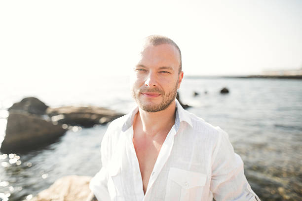 istock handsome model man posing on stone by the sea 604826824