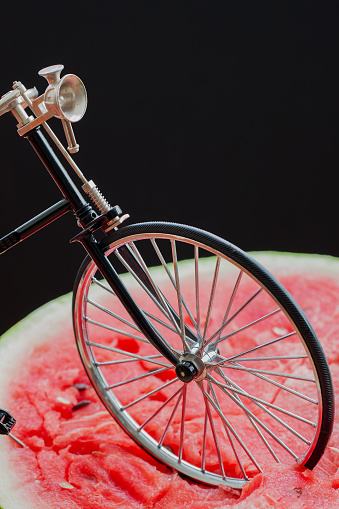 Front wheel retro vintage bicycle standing on top of a large cut in half scarlet ripe watermelon, top view, close-up, vertical