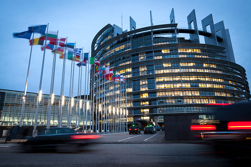 Strasbourg, France - October 24, 2013: Entrance of the main building of European Parliament in Strasbourg.  Completed in 1999 the building is the seat of the European Parliament (other work places are Luxembourg and Brussels). It was named after Louise Weiss (1893 – 1983) which was a French author, journalist, feminist and European politician. Some taxis and pedestrians in the foreground