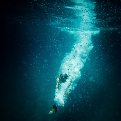 Underwater shot of a diver after the jump in the sea and breaking water surface. This photo contains noise as a result of very low light conditions