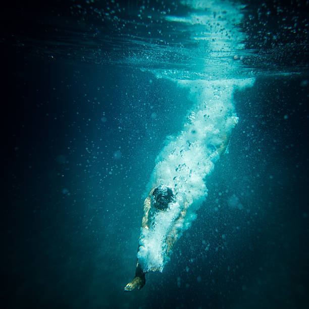 Underwater action shot of diver breaking water surface Underwater shot of a diver after the jump in the sea and breaking water surface. This photo contains noise as a result of very low light conditions diving into water stock pictures, royalty-free photos & images