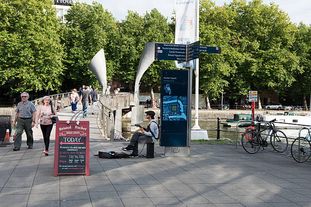 Bristol busker Bristol, UK - September 14, 2016: Bristol busker. This busker at Pero's bridge, Bristol harbourside, is playing jazz guitar while crowds cross the footbridge on this Summer's day. Bristol's floating harbour can be seen behind him. Live music in all its forms is a major feature of Bristol life. chat gpt nederlands stock pictures, royalty-free photos & images