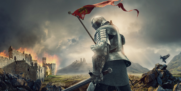 Caballero medieval con estandarte y espada de pie cerca del castillo en llamas photo