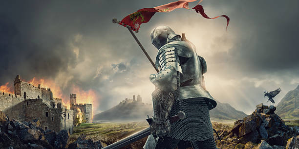 Medieval Knight With Banner and Sword Standing Near Burning Castle A medieval knight from rear view standing hold a sword and tattered flag, and looking behind himself. The warrior knight is wearing a suit of armour and chainmail, and walks on rocky ground close to a burning ruin of a castle under stormy and dramatic evening sky.  arthurian legend stock pictures, royalty-free photos & images