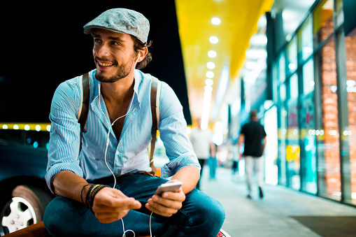 Handsome hipster businessman listening music by the shopping mall at night, and singing a little.