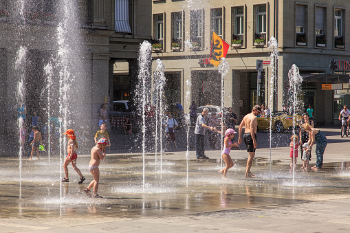 Bern, Switzerland - 11 June, 2014: people with children playing in fountains on Bundesplatz square on a hot summer day. The city of Bern is the capital of Switzerland and the fourth most populous city in the country.
