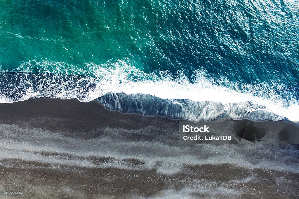 Aerial tracking shot Cold ocean waves washing down the black sand beach making a lot of ocean foam. The video is taken by drone which goes down to 350 meters and rotates. Beach Stock Photo