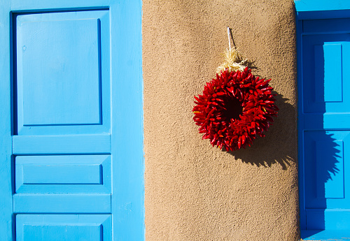Santa Fe style: A red chili pepper ristra wreath hangs on an adobe wall next to a blue shutter/door. Ristras on doors are not just decorative in New Mexico, but are believed to ward off evil.