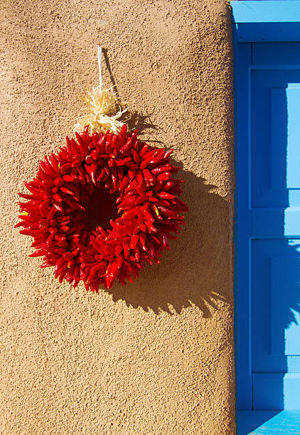 santa fe stil: chili pfeffer kranz, adobe wand, blaues fenster - wreath chili pepper pepper ristra stock-fotos und bilder