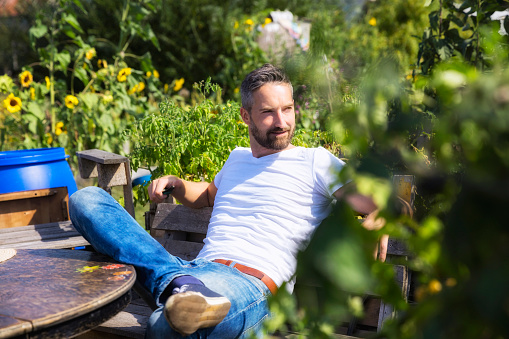 man resting on wooden bench against plants in yard