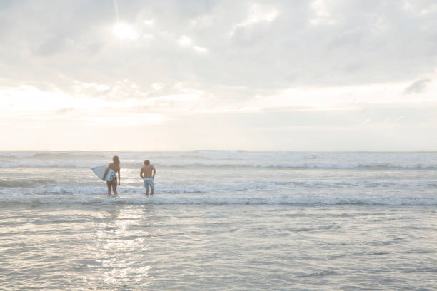 istock Surf instructor heads into surf with young woman 605390985