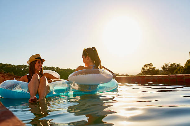 Friends in inflatable ring floating on pool Happy female friends in inflatable ring floating on swimming pool during summer vacation pool raft stock pictures, royalty-free photos & images