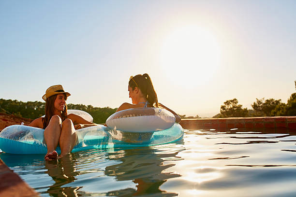 friends in inflatable ring floating on pool - poolside стоковые фото и изображения