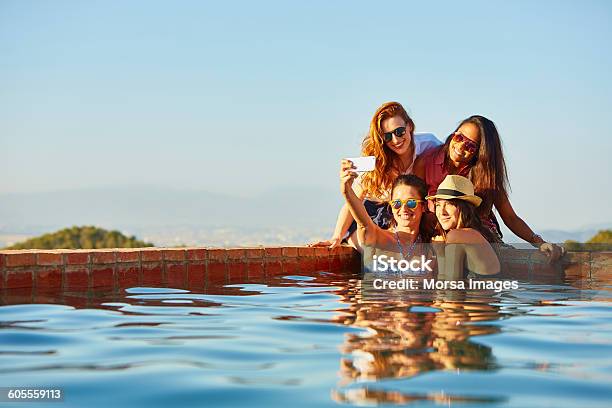 Female Friends Taking Self Portrait At Pools Edge Stock Photo - Download Image Now - Vacations, Friendship, Summer