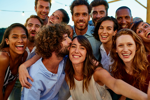 Portrait of happy young woman taking selfie with friends during social gathering