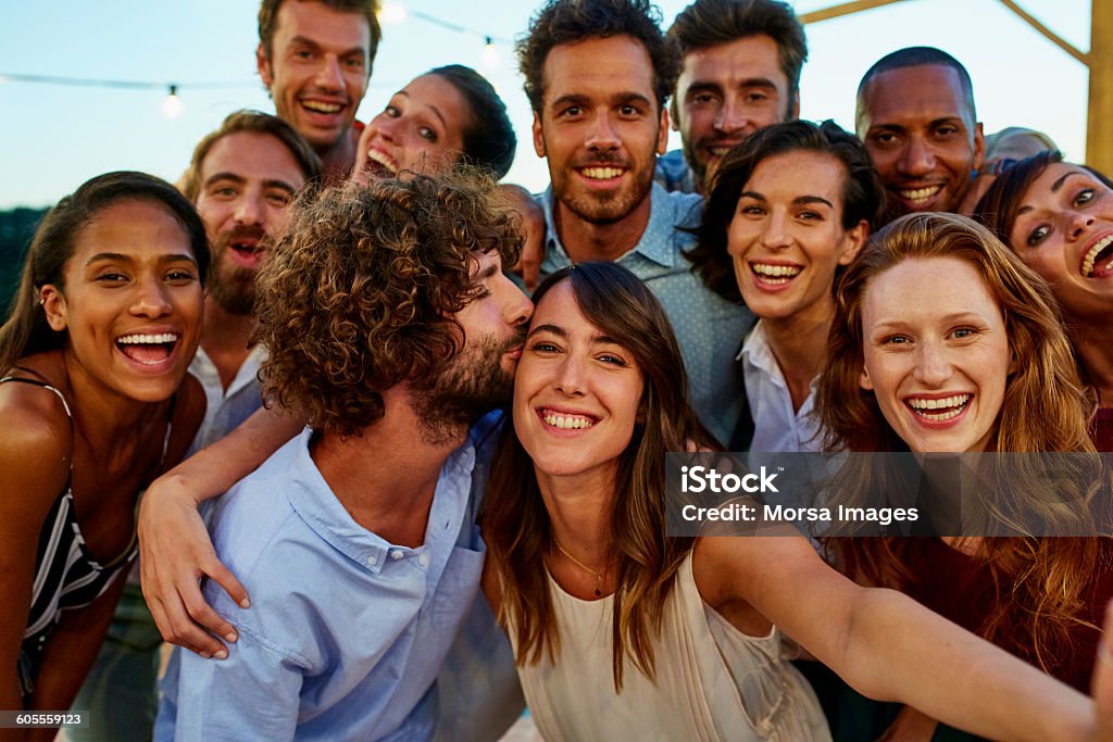 Happy woman taking selfie with friends Portrait of happy young woman taking selfie with friends during social gathering Friendship Stock Photo