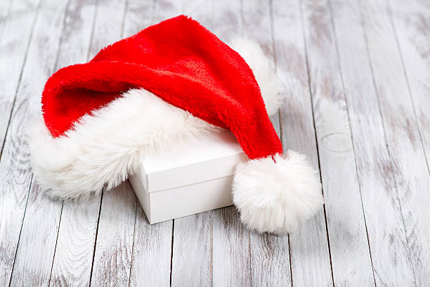 istock Santa Claus hat over gift box on wooden background. 605737410
