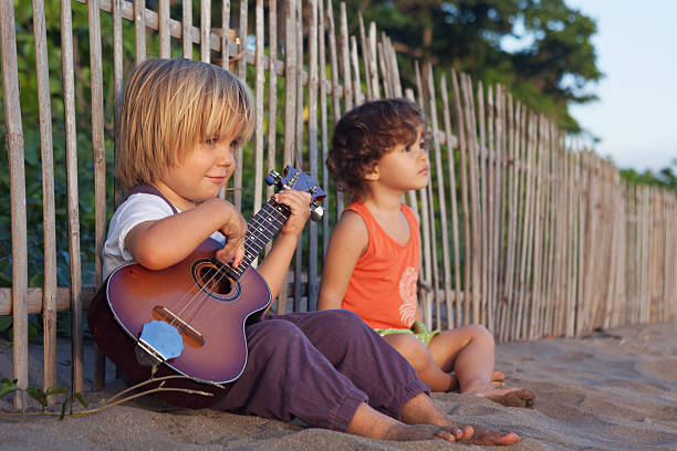 Little children have fun on sunset tropical beach. Little happy boy have fun, play music on Hawaiian guitar ukulele for small baby girl, enjoying sunset ocean beach. Children healthy lifestyle. Travel, family activity on tropical island summer holiday big island hawaii islands photos stock pictures, royalty-free photos & images