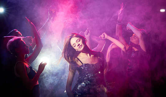 Young woman with closed eyes dancing among crowd at night club
