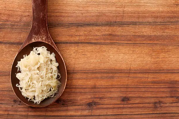Top view of wooden spoon over table with sauerkraut on it