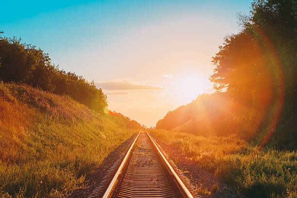 istock Railway Going Straight Ahead Through Summer Hilly Meadow To Sunset 605752530