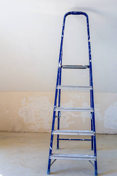 istock Blue dirty stepladder at plaster wall background 605753018