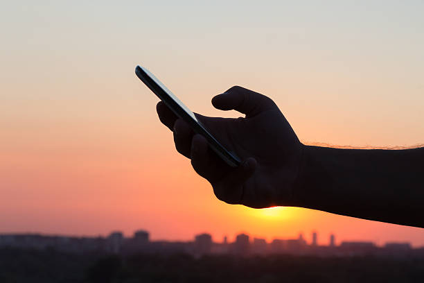 istock Male hand using smart phone at sunset 605755422