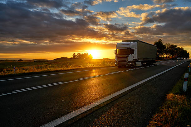 istock White truck driving on asphalt road during a dramatic sunset. 605757130
