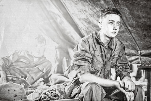 Joven soldado de infantería de la Segunda Guerra Mundial sentado en una cuna en su tienda de campaña photo