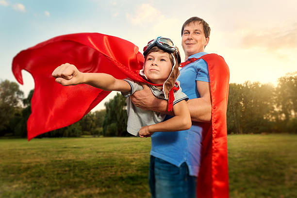 padre e figlio che giocano in costume da supereroe parcheggiano su natu - action family photograph fathers day foto e immagini stock