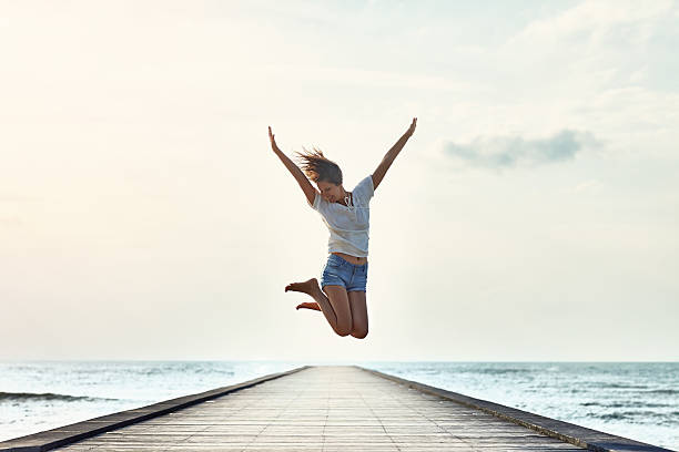 chica feliz saltando en el muelle - jumping freedom women beach fotografías e imágenes de stock