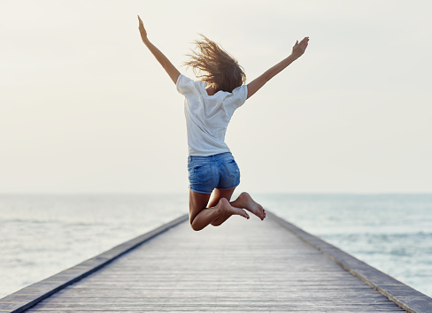 Back view of jumping girl on the pier. Freedom concept