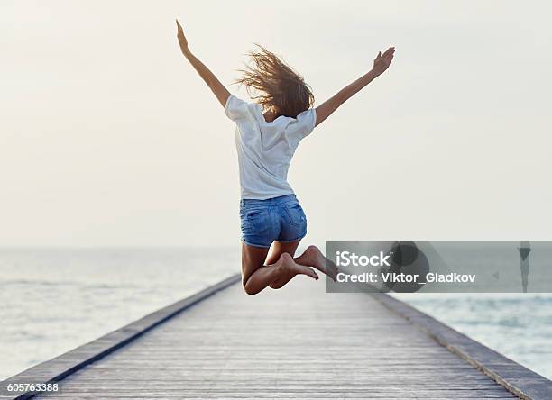 Back View Of Jumping Girl On The Pier Stock Photo - Download Image Now - Women, Happiness, Jumping