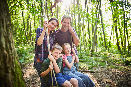 Portrait smiling family at rope swing in woods